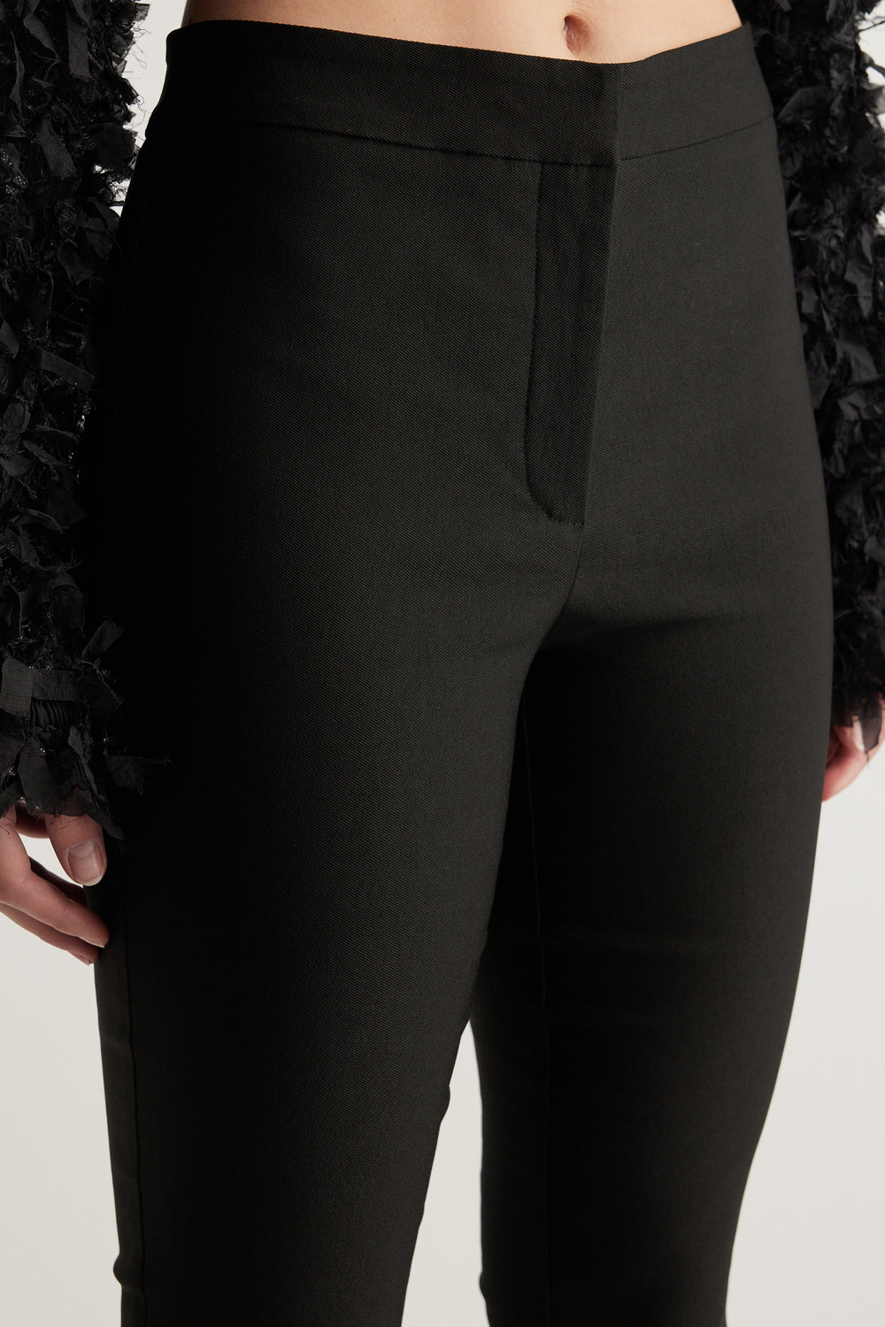 Close-up of a woman wearing black slim leg pants with a mid rise waist and zip fly closure
