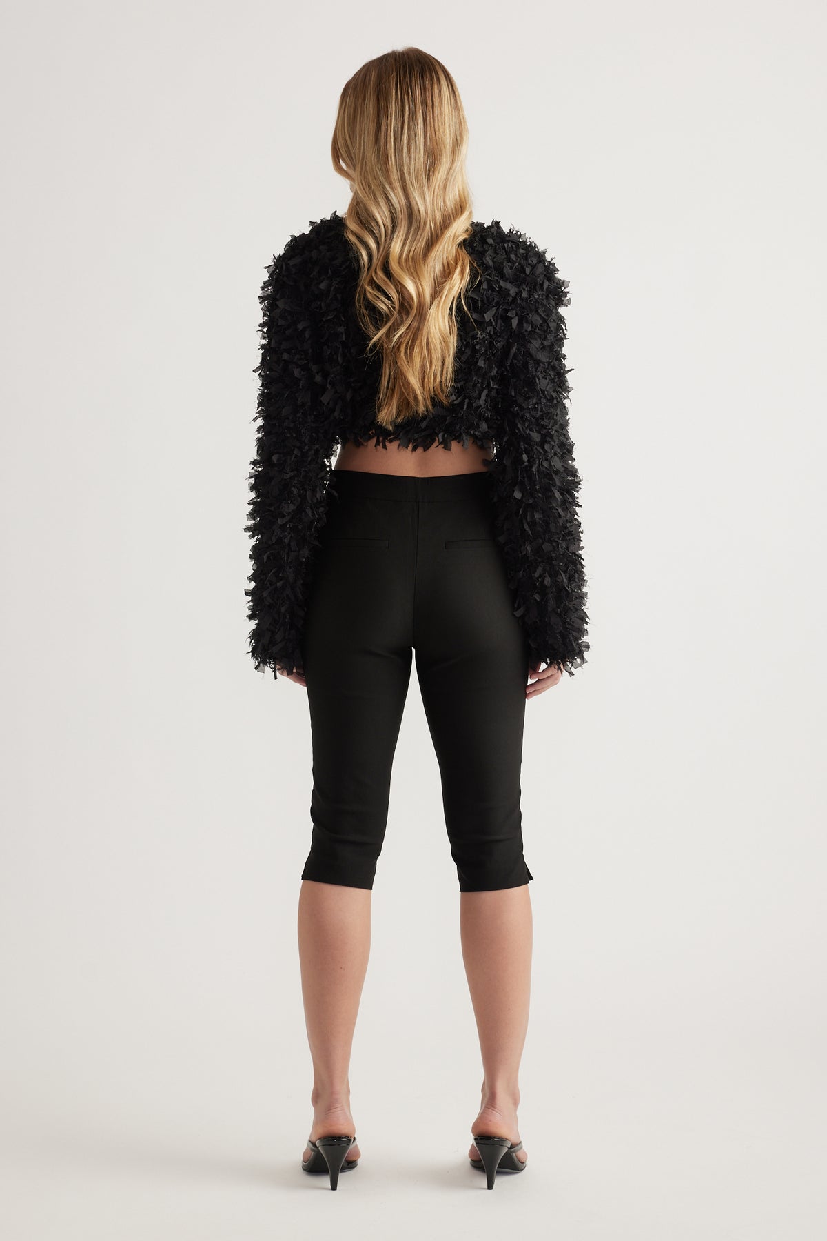 Back view of woman wearing black slim fit capri pants with a cropped textured jacket