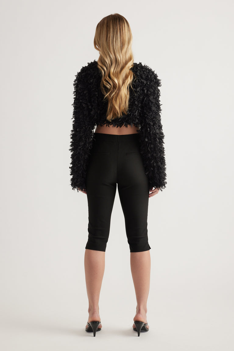 Back view of woman wearing black slim fit capri pants with a cropped textured jacket