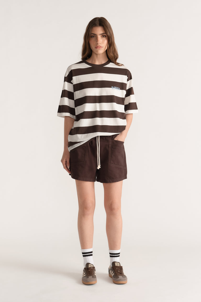 Model wearing brown pull on denim shorts with a drawstring, striped oversized tee and sneakers