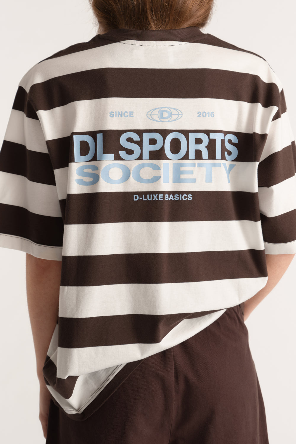 Back view of a relaxed brown and cream striped tee with a blue D Luxe Sports Society graphic