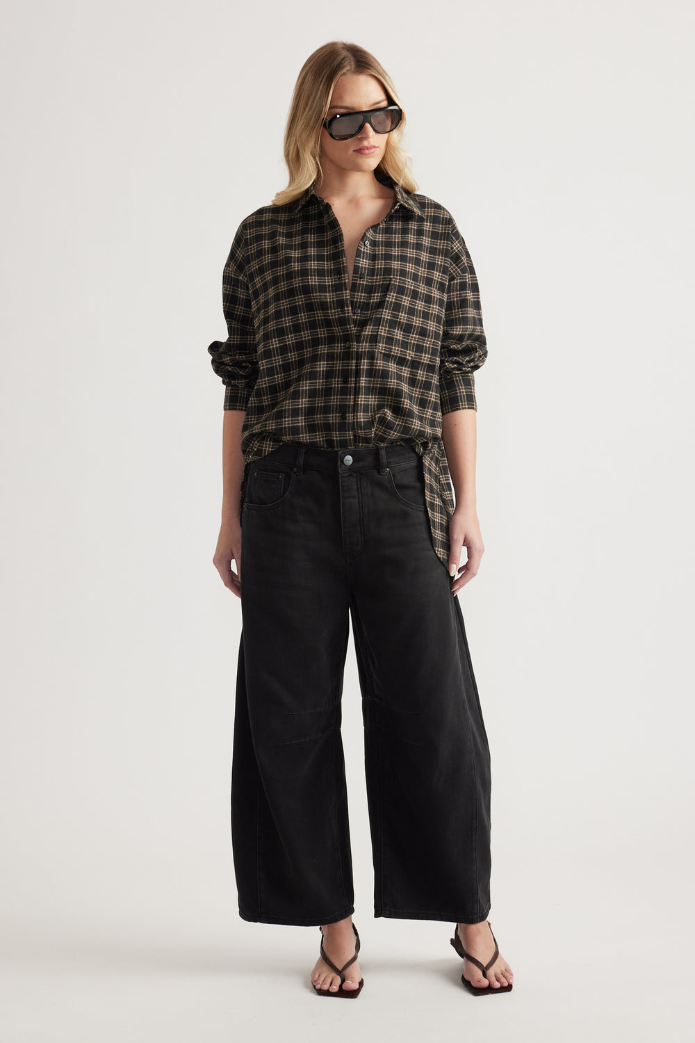 Woman wearing oversized black and brown checked shirt paired with wide-leg black denim pants and sandals