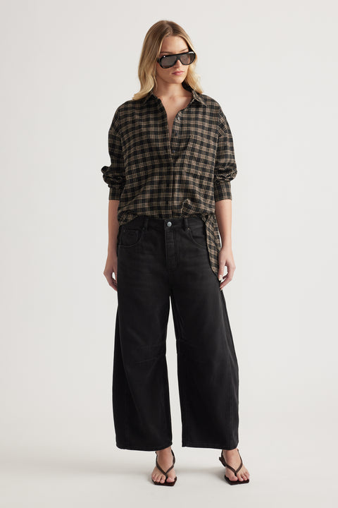 Woman wearing oversized black and brown checked shirt paired with wide-leg black denim pants and sandals