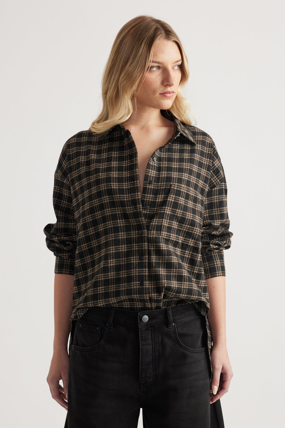 Woman wearing oversized black and tan checked flannel shirt with front pocket and black jeans