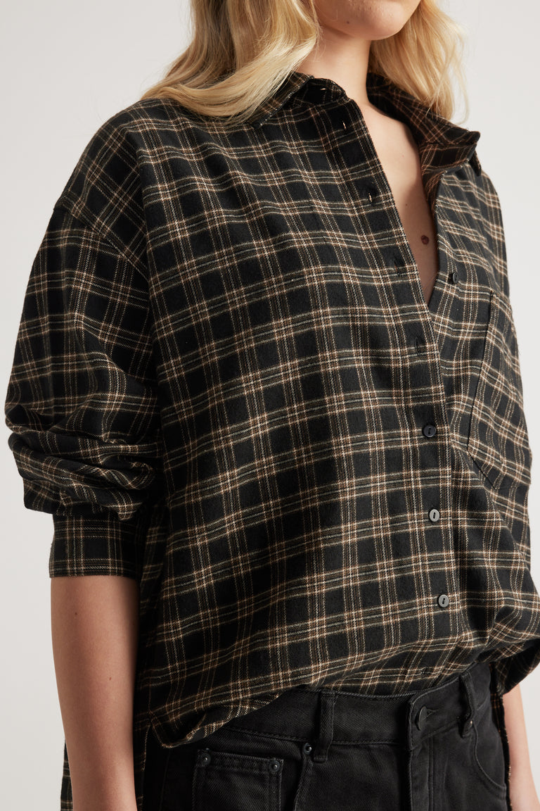 Close-up of a woman wearing an oversized black and beige check flannel shirt with rolled-up sleeves and black jeans