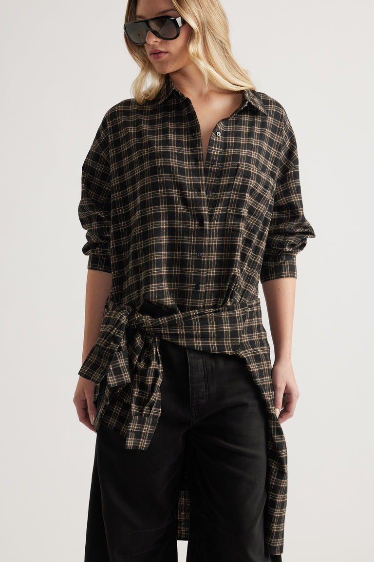 Woman wearing oversized black and beige checked flannel shirt tied at waist with long sleeves and black pants