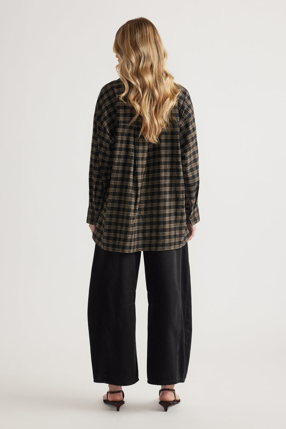 Rear view of woman wearing oversized plaid flannel shirt with long sleeves paired with wide-leg black pants and heels