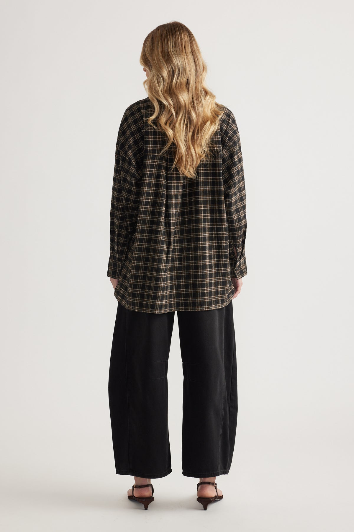 Rear view of woman wearing oversized plaid flannel shirt with long sleeves paired with wide-leg black pants and heels