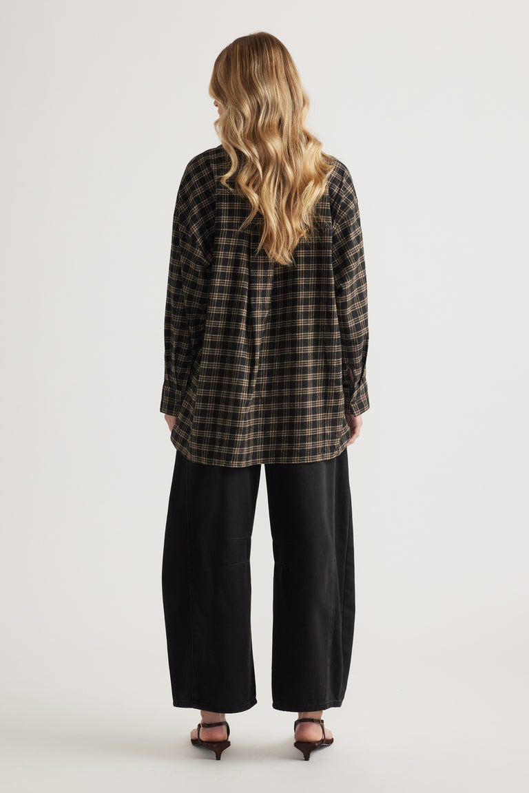Rear view of woman wearing oversized plaid flannel shirt with long sleeves paired with wide-leg black pants and heels