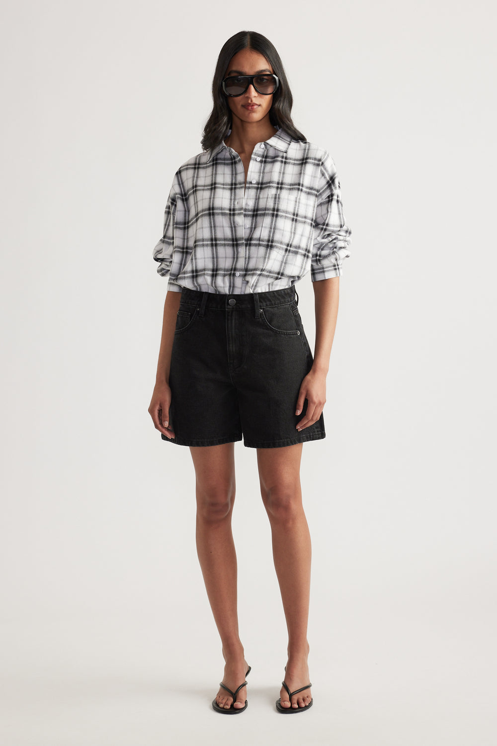 Woman wearing oversized white and black check flannel shirt with black high-waisted denim shorts and sandals