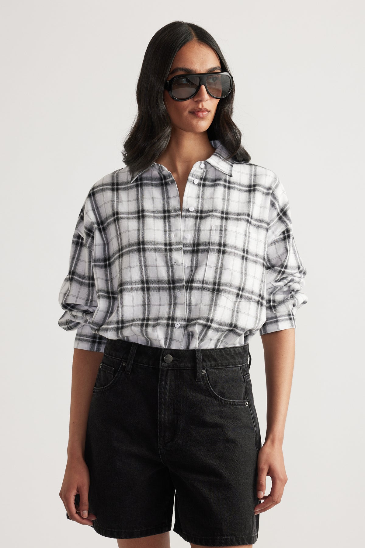 Woman wearing oversized black and white plaid shirt with rolled sleeves paired with black high-waisted denim shorts