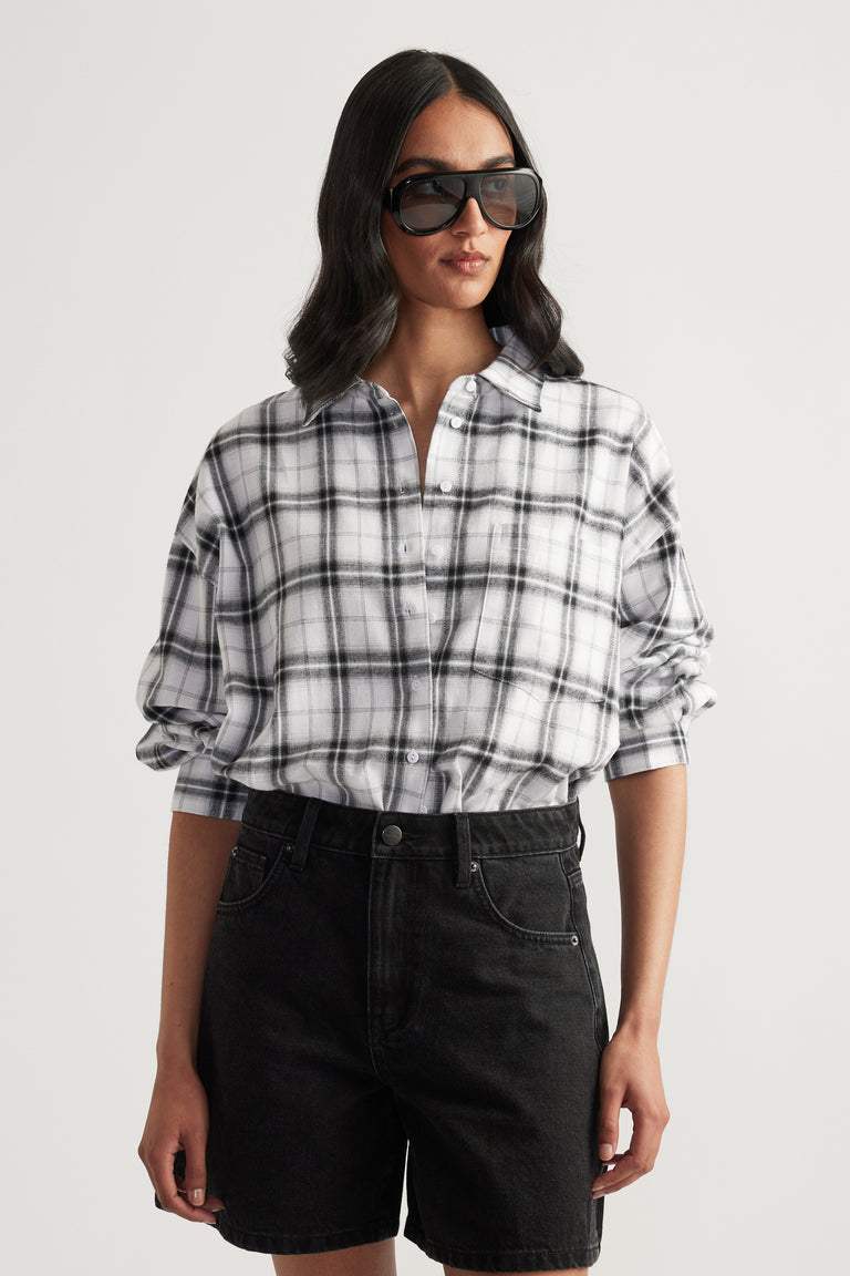 Woman wearing oversized black and white plaid shirt with rolled sleeves paired with black high-waisted denim shorts