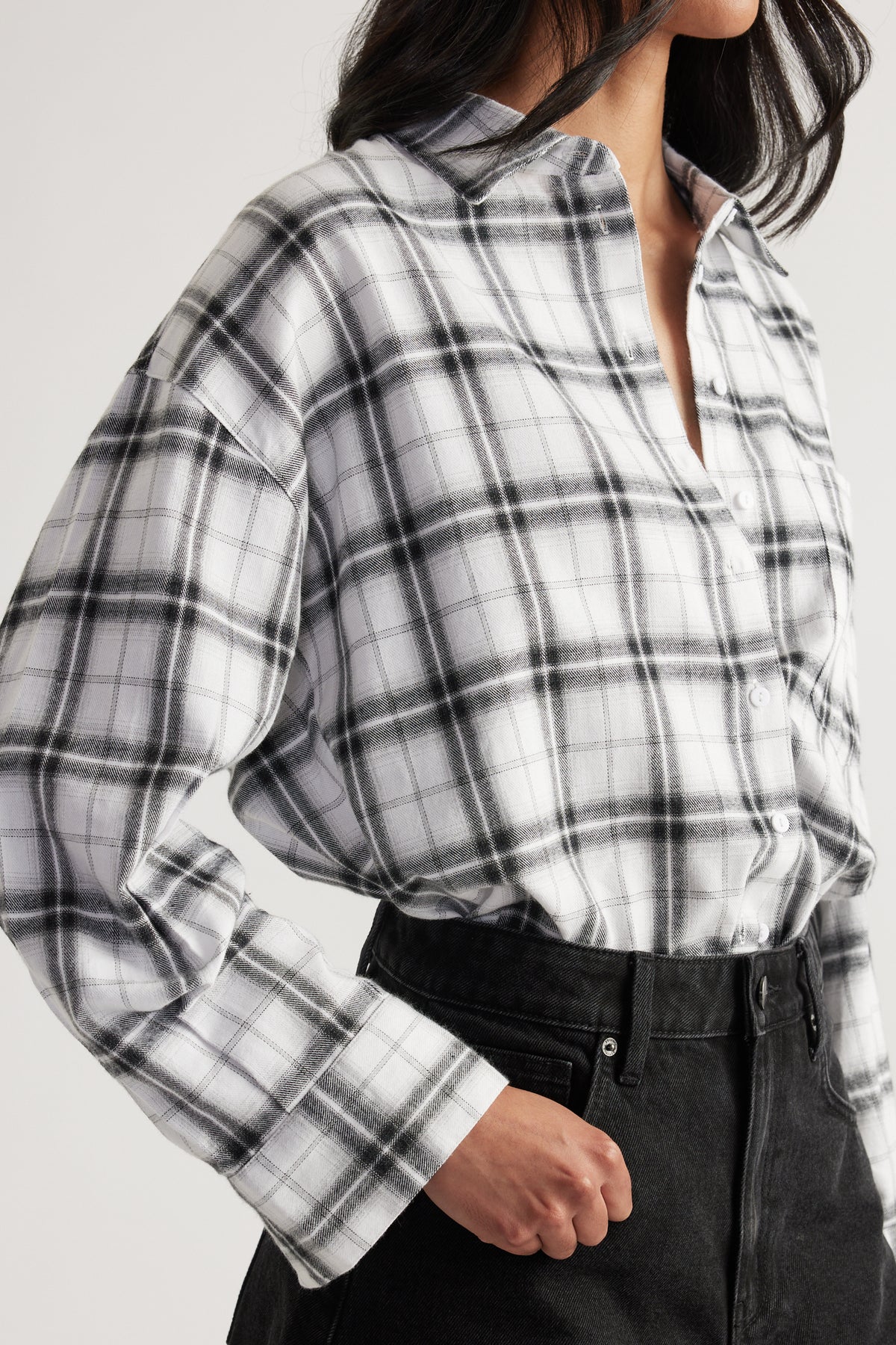 Close-up of woman wearing black and white plaid oversized flannel shirt tucked into high-waisted black jeans