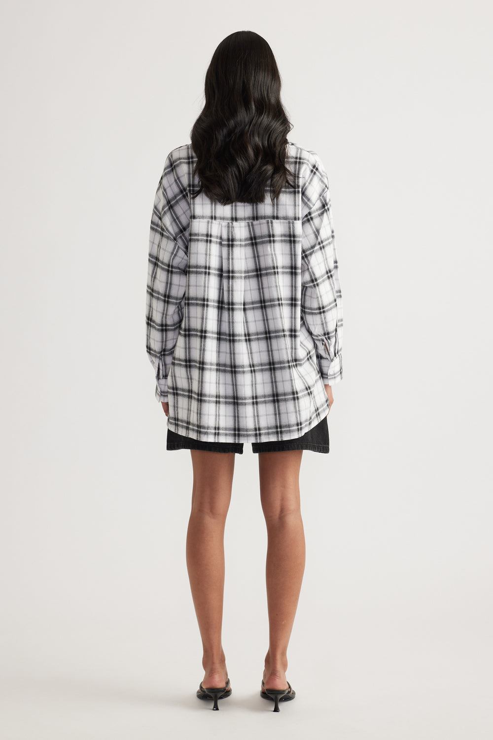 Rear view of woman wearing oversized black and white check flannel shirt paired with black shorts and heeled sandals