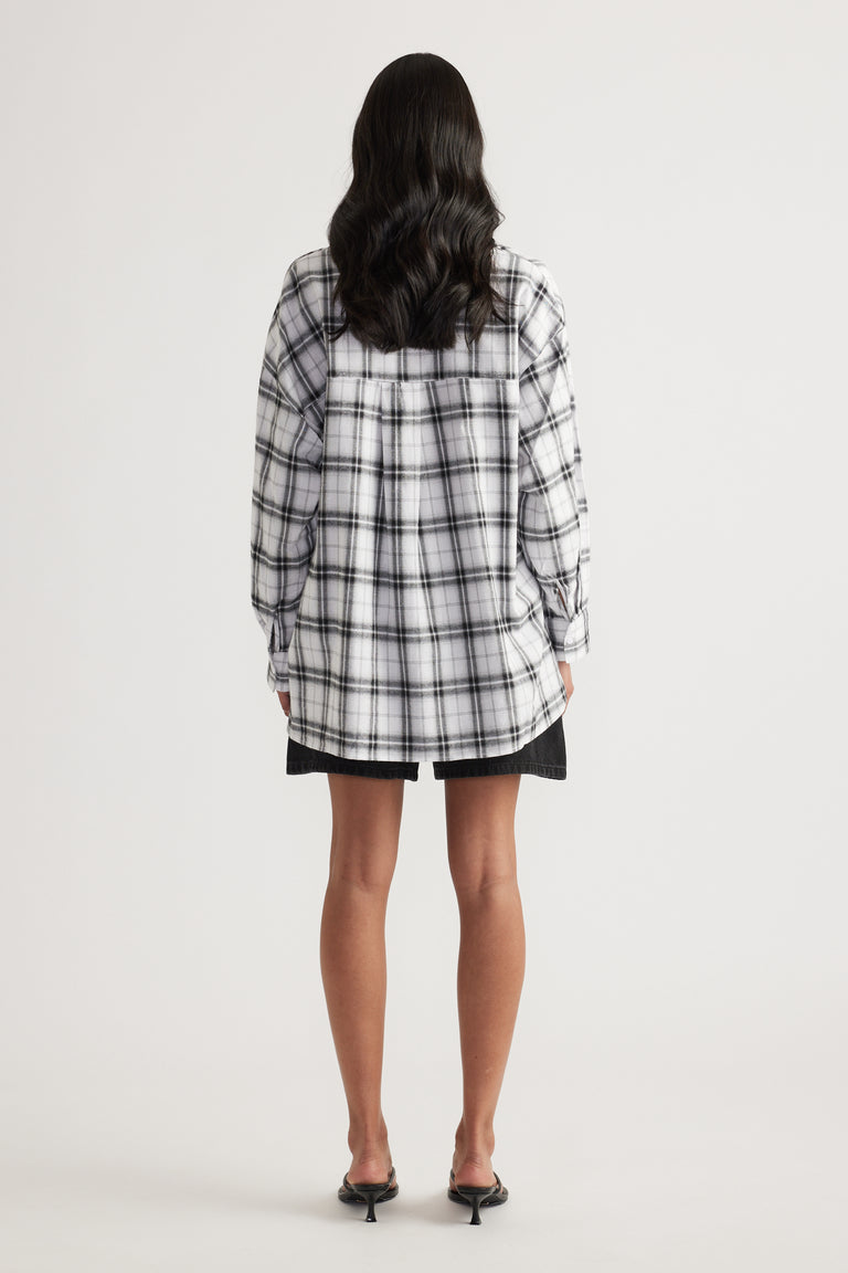 Rear view of woman wearing oversized black and white check flannel shirt paired with black shorts and heeled sandals