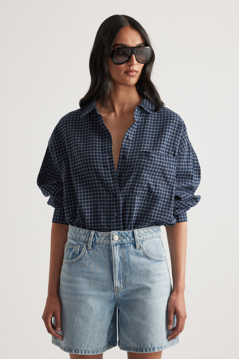 Woman wearing oversized navy checkered flannel shirt paired with light wash high-rise denim shorts and sunglasses