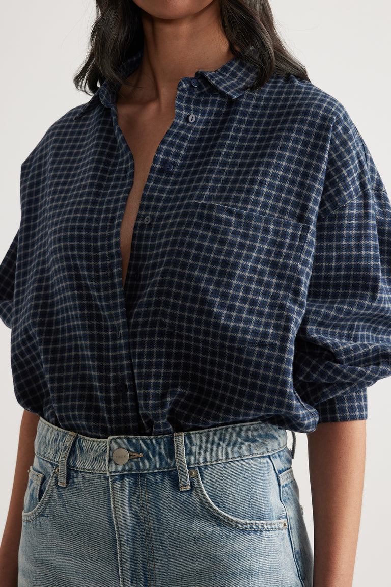 Woman wearing a relaxed fit navy check flannel shirt with rolled sleeves tucked into high-rise light wash denim jeans