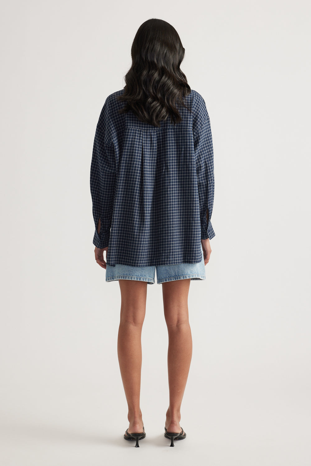 Rear view of a woman wearing an oversized navy check flannel shirt with light blue denim shorts and black heels