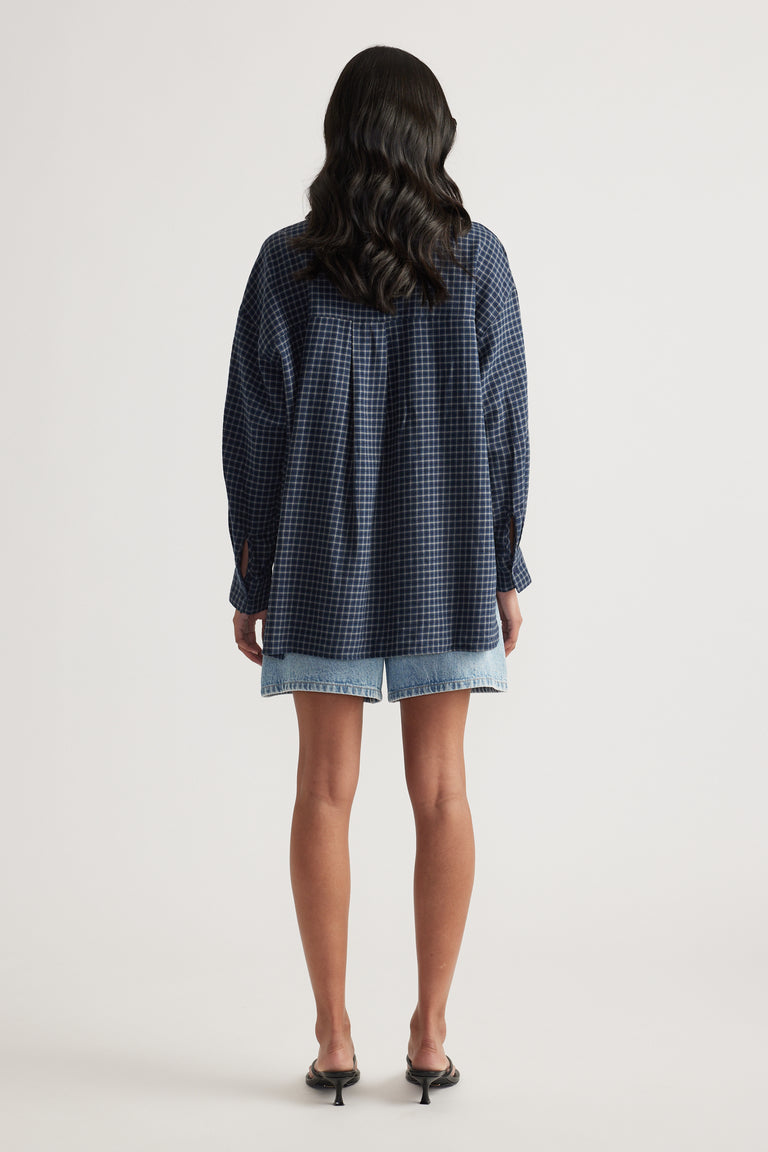 Rear view of a woman wearing an oversized navy check flannel shirt with light blue denim shorts and black heels