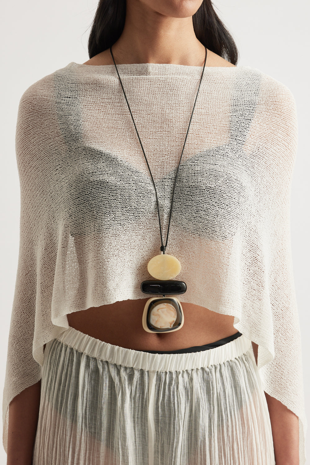 Woman wearing a statement cord necklace with three large pebble beads over a sheer cream knit top