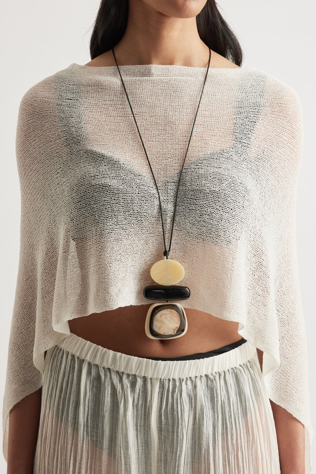 Woman wearing a statement cord necklace with three large pebble beads over a sheer cream knit top
