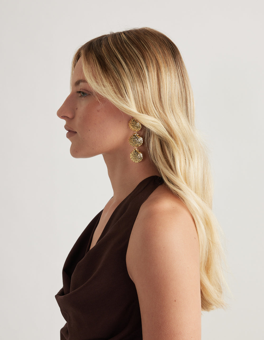 Profile of a woman wearing large three-tiered beaten gold shell drop earrings