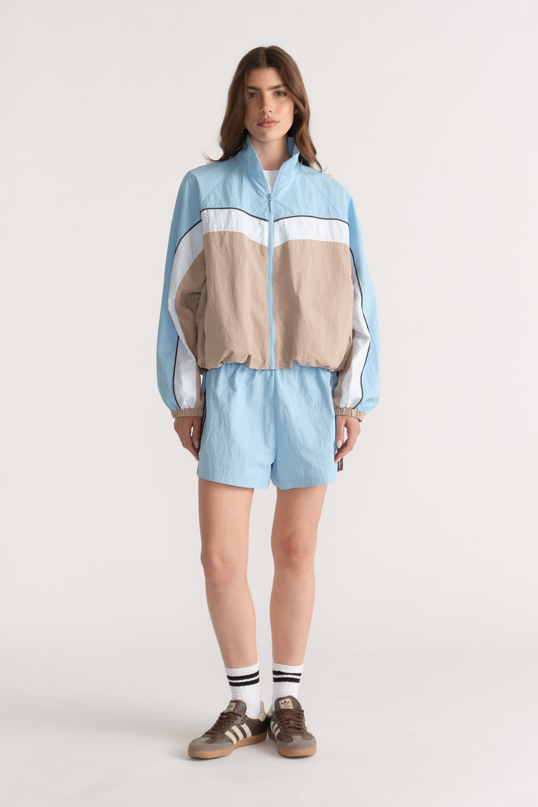 Woman wearing a light blue and beige colour block funnel neck jacket with matching shorts and sneakers
