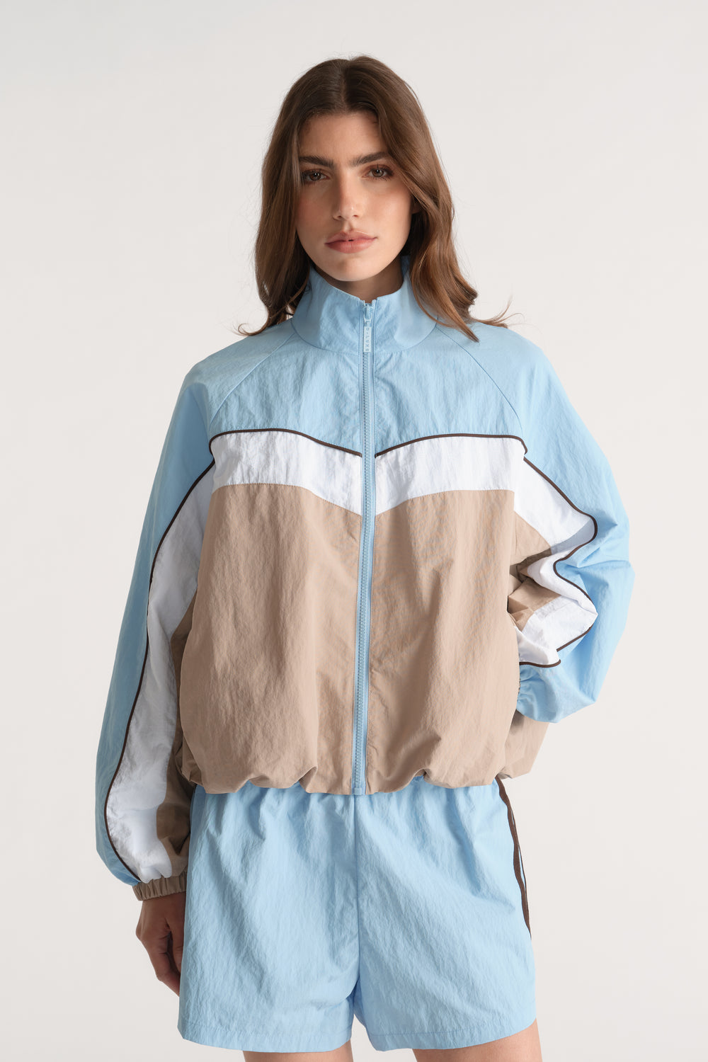 Woman wearing a light blue, white and beige colour block zip jacket with matching shorts