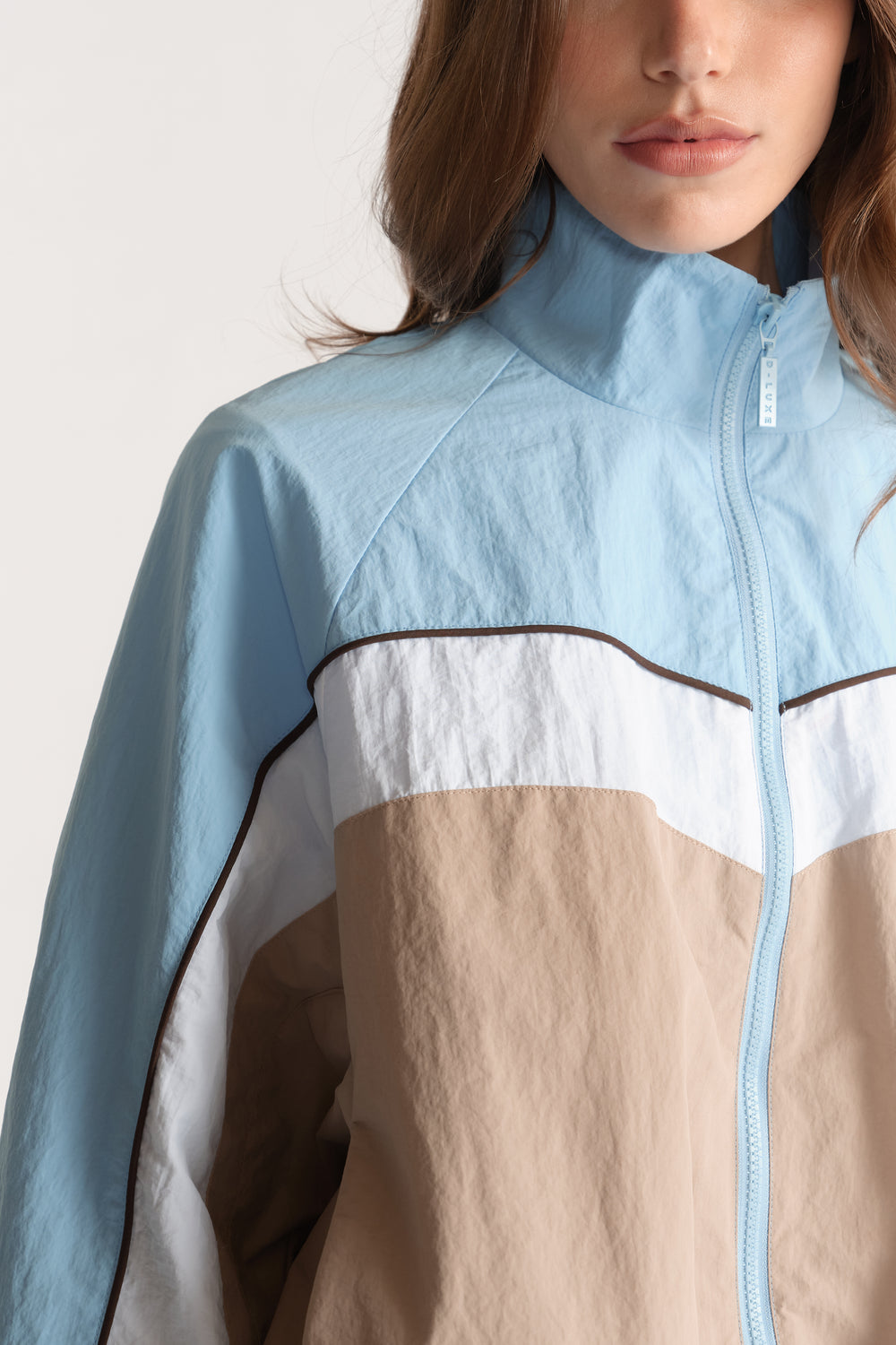 Woman wearing a light blue, white and beige colour block funnel neck jacket with a front zip closure