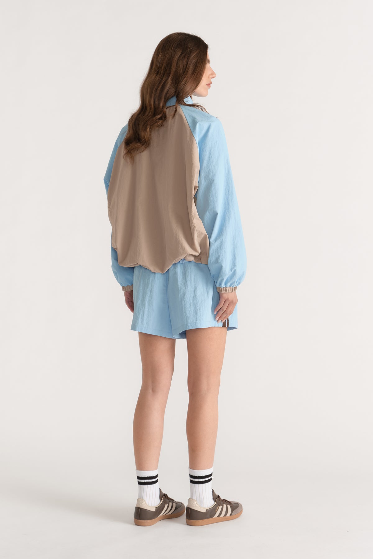 Woman wearing a light blue and taupe spliced spray jacket with matching shorts and sneakers