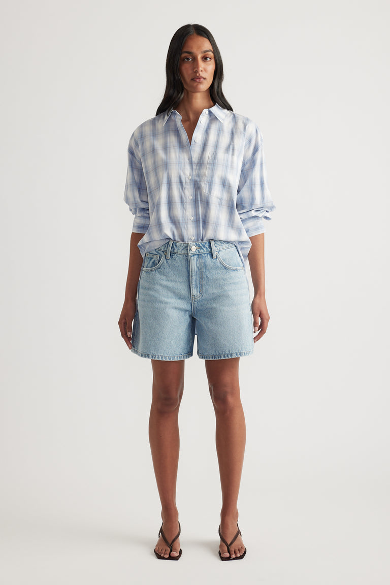 Woman wearing an oversized blue checked shirt with rolled sleeves, denim shorts and strappy sandals