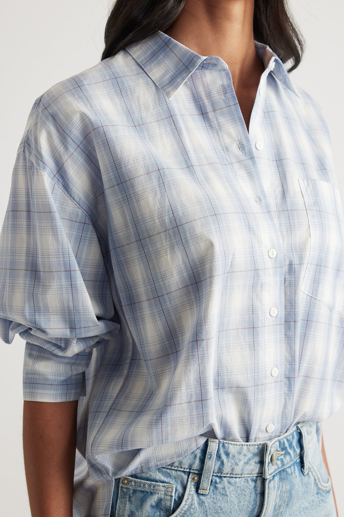 Woman wearing an oversized light blue plaid button through shirt with rolled sleeves and jeans