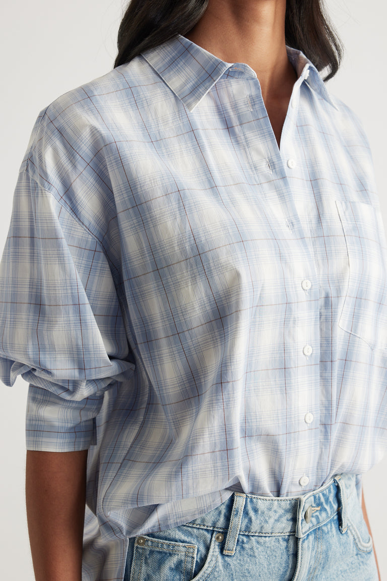 Woman wearing an oversized light blue plaid button through shirt with rolled sleeves and jeans