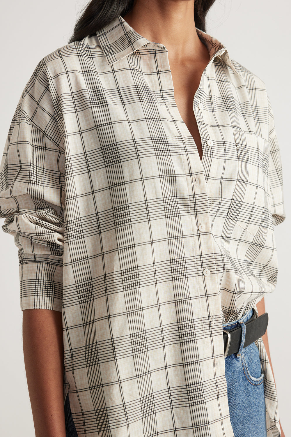 Woman wearing an oversized cream plaid shirt with a collar, patch pocket and rolled sleeves, styled with blue jeans