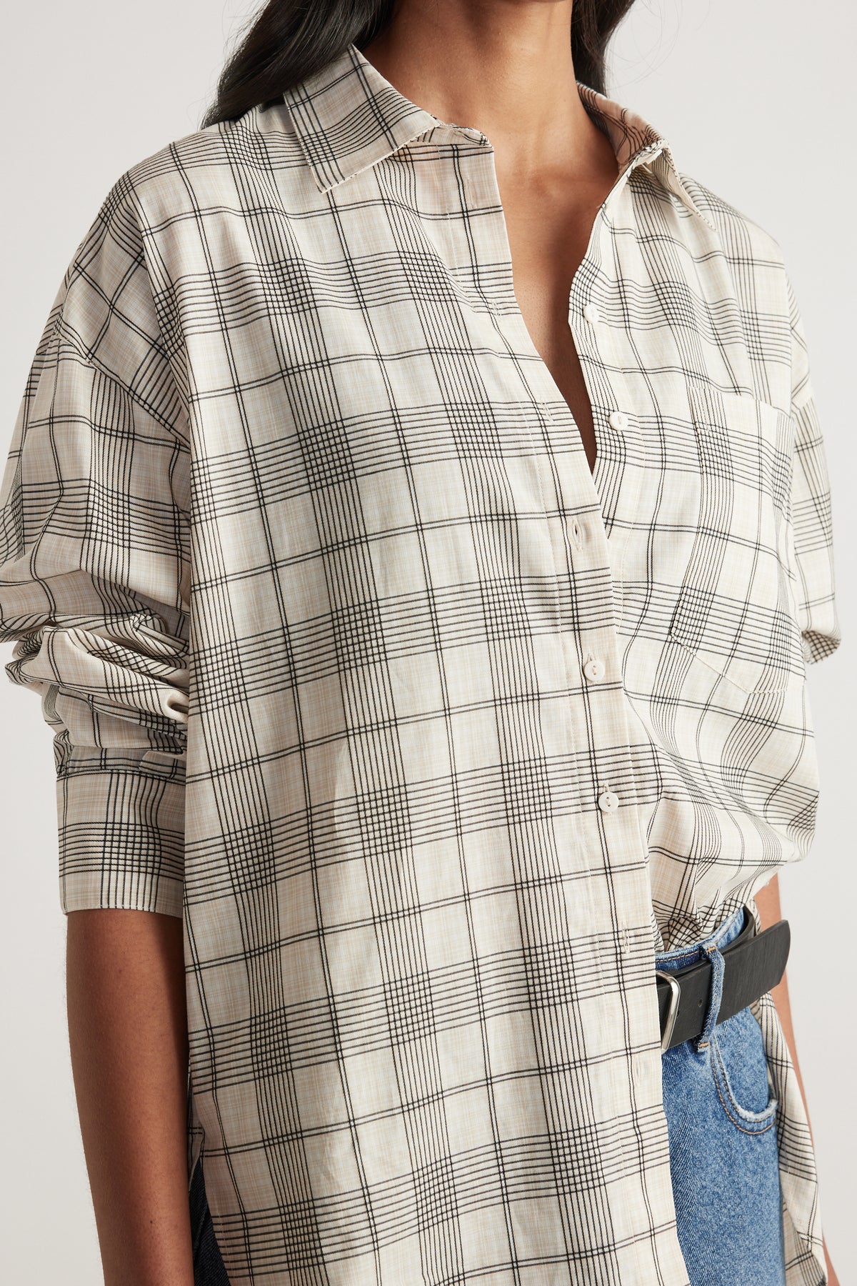 Woman wearing an oversized cream plaid shirt with a collar, patch pocket and rolled sleeves, styled with blue jeans