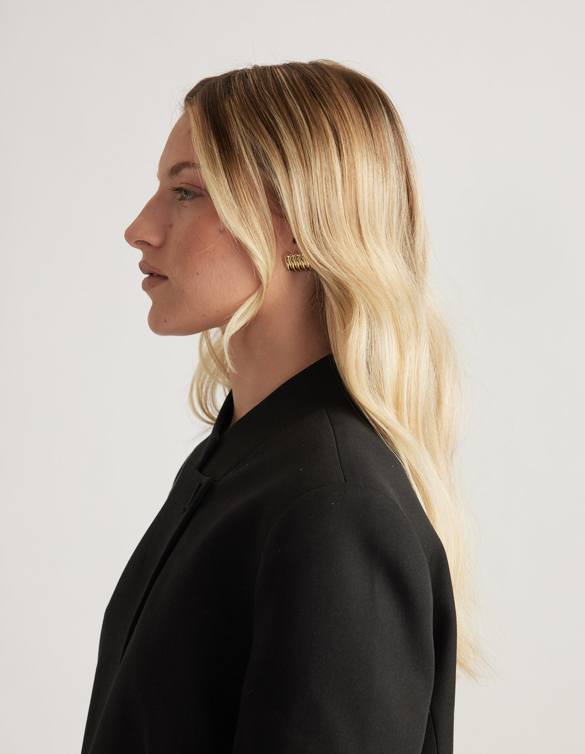 Woman in profile wearing a black blazer with a gold ribbed stud earring and long blonde hair