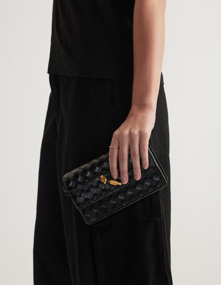 Delicate gold single band ring worn with a black woven clutch and relaxed black outfit