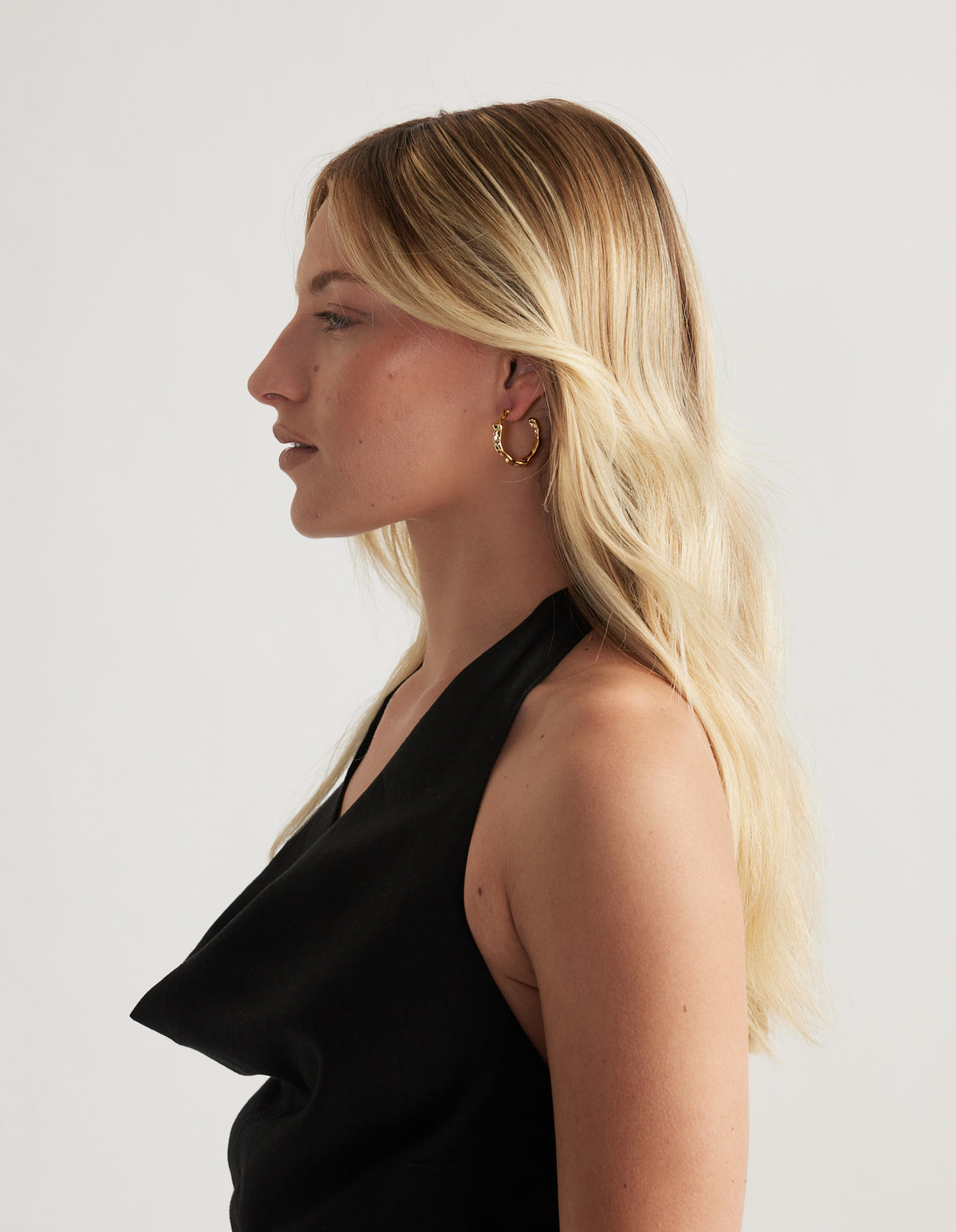 Woman in profile wearing a gold twisted hoop earring and black halter top