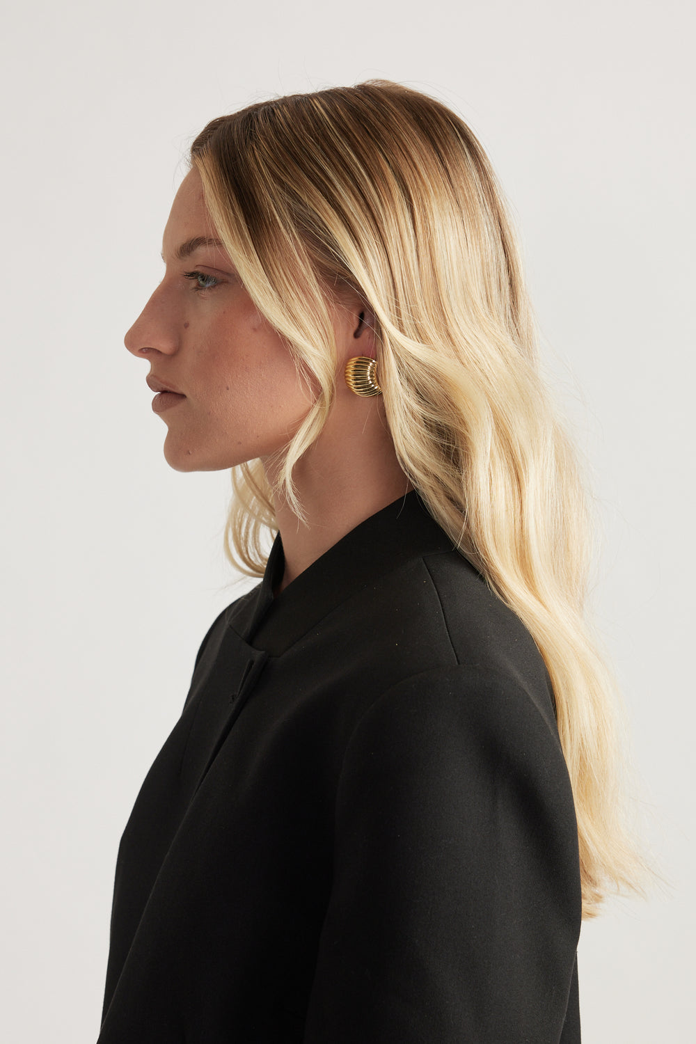 Woman in profile wearing a gold ribbed statement earring with a black blazer