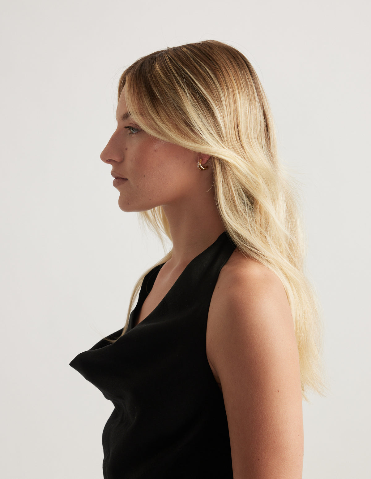 Woman in profile wearing a small gold diamante earring with long blonde hair and a black top