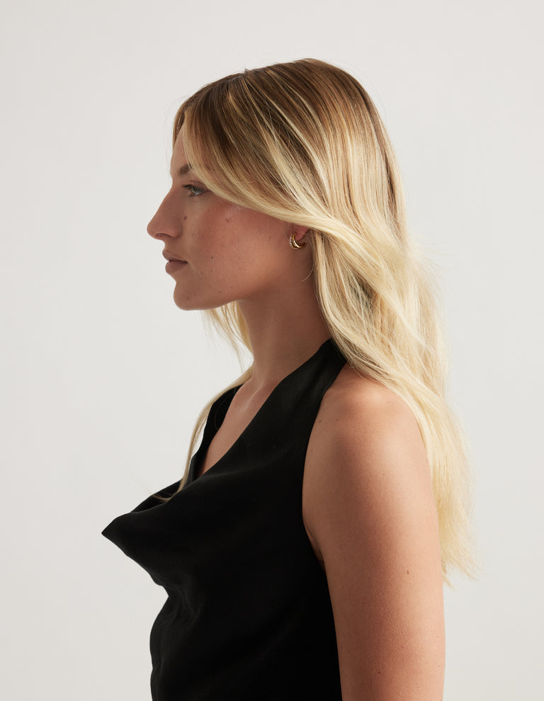 Woman in profile wearing a small gold diamante earring with long blonde hair and a black top
