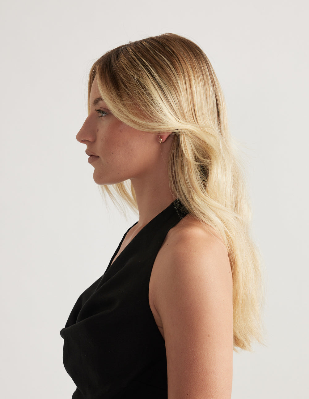 Woman in profile with long blonde hair wearing a small gold diamante stud earring and black top