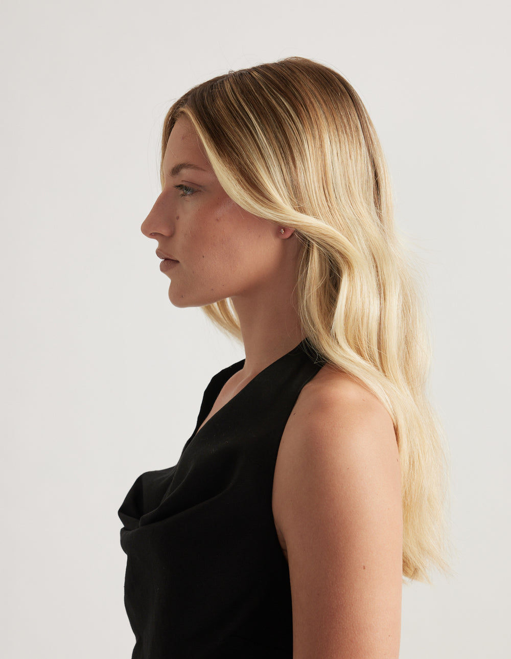 Woman in profile wearing a small gold stud earring, with long blonde hair and a black top