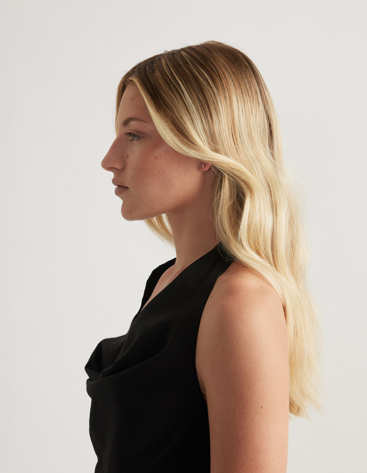 Woman in profile wearing a small gold stud earring, with long blonde hair and a black top