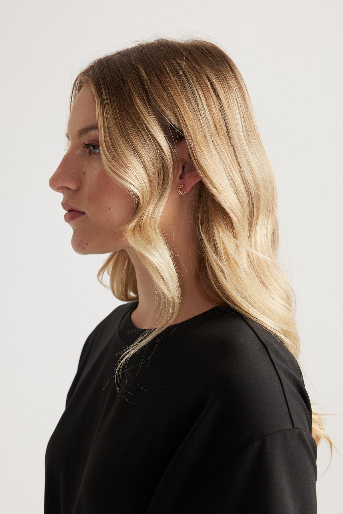 Side profile of a woman wearing a black top and small gold hoop earring