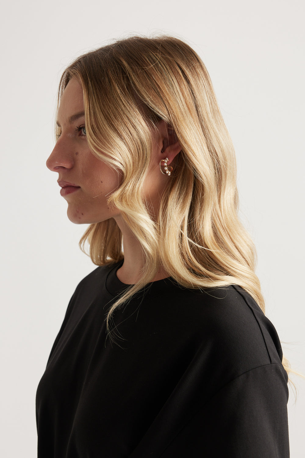 Woman in profile wearing gold mini hoop earrings and a black top