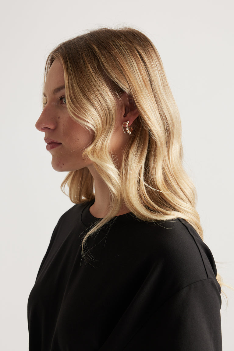 Woman in profile wearing gold mini hoop earrings and a black top