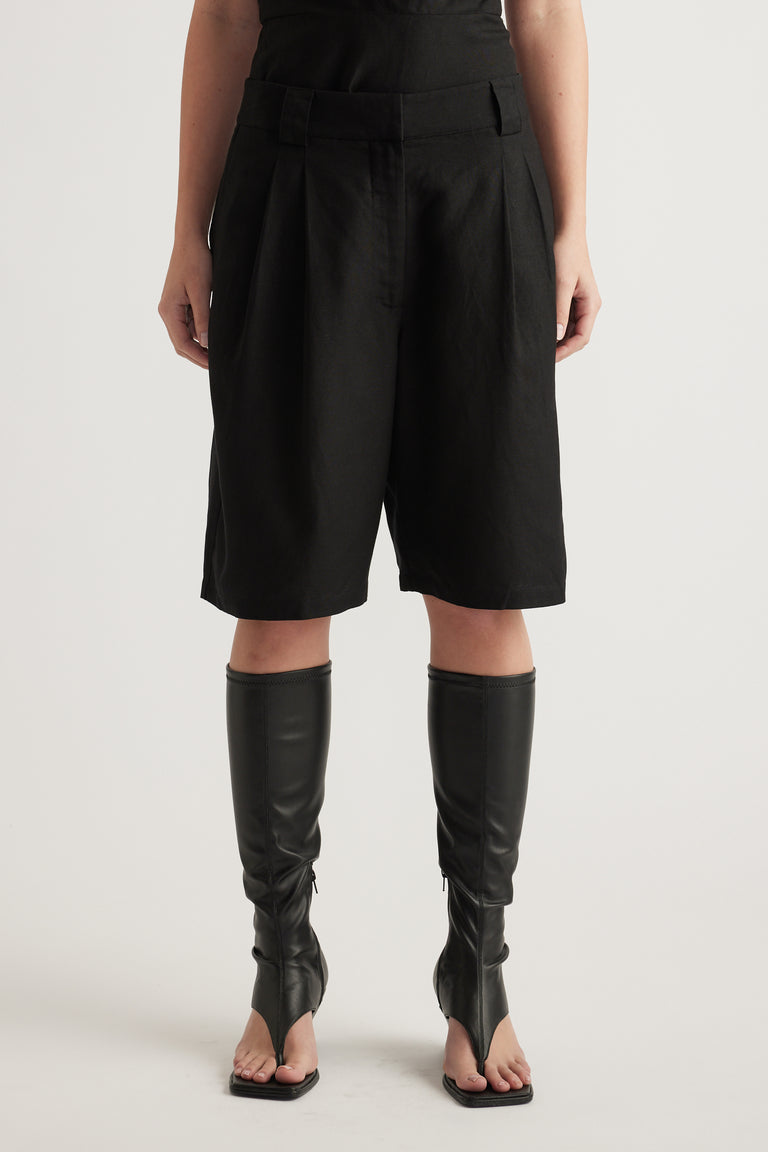 Model wearing black pleated shorts with a mid-rise waist and above-knee hem