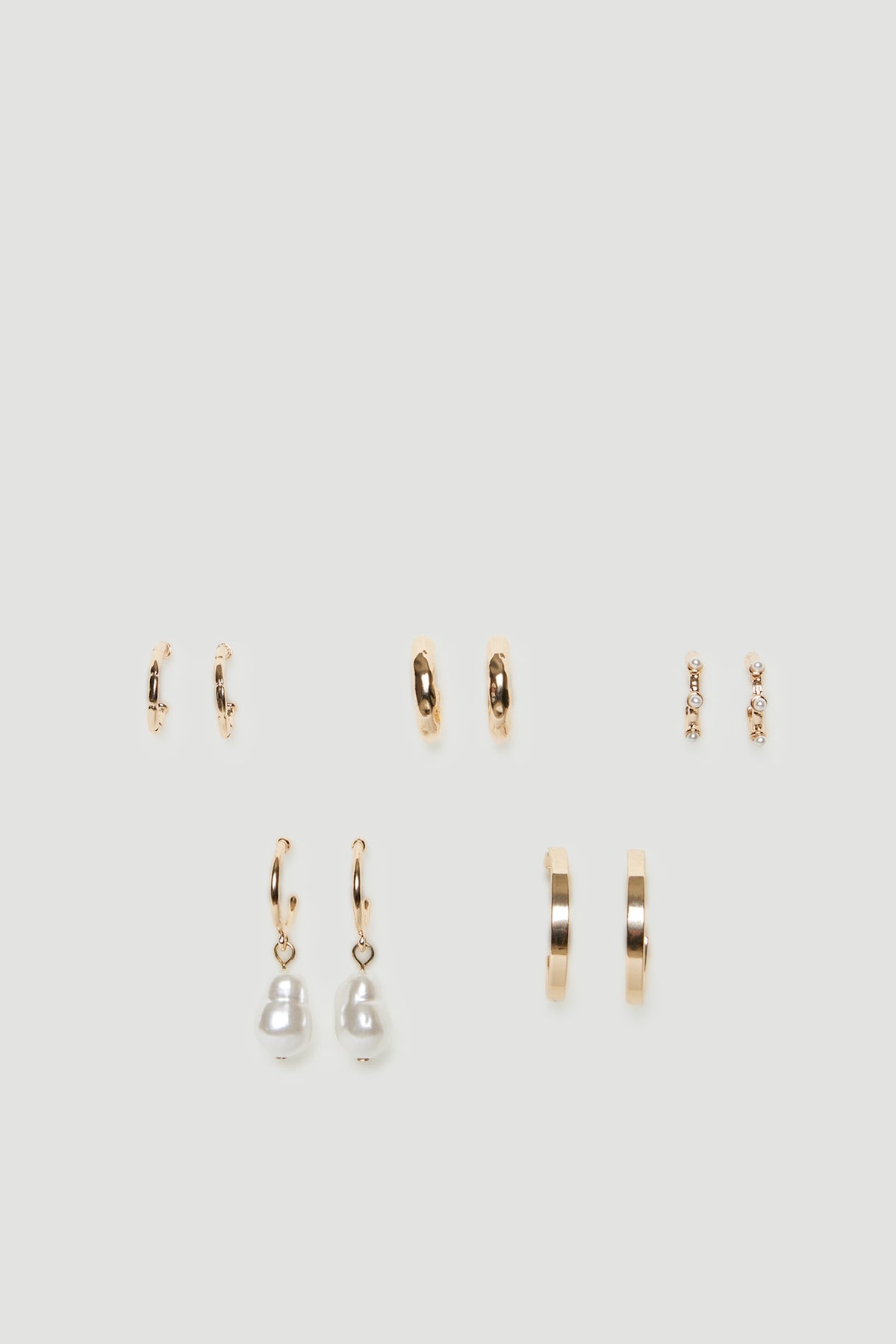 Five pairs of gold tone mini hoop earrings with textured finishes and pearl details
