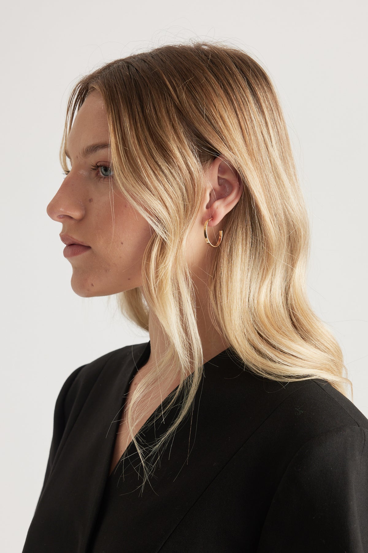 Side profile of a woman wearing a small gold hoop earring with a black top